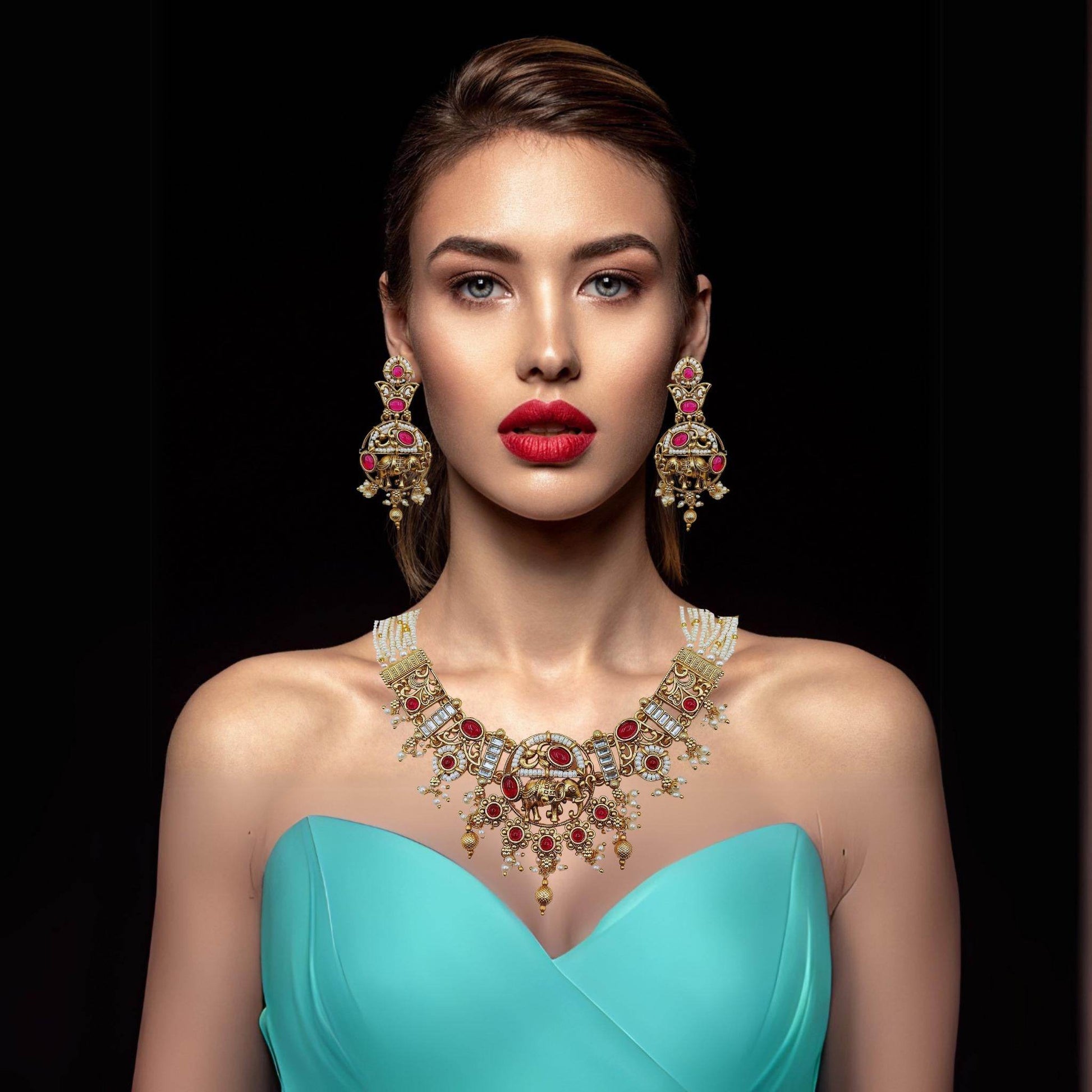 Model wearing Rajputi elephant design necklace set with red stones and matching earrings in gold finish